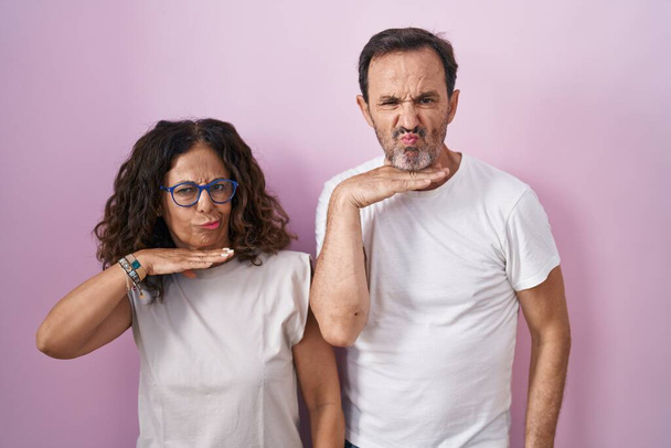 Испанская пара средних лет вместе на розовом фоне перерезает горло рукой, как нож, угрожает агрессией яростным насилием  - Фото, изображение