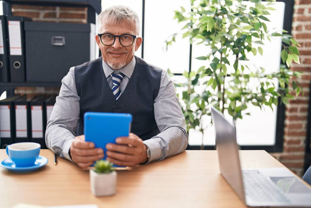 Średni wiek siwowłosy mężczyzna pracownik biznesu za pomocą touchpad w biurze - Zdjęcie, obraz