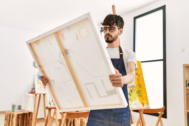 Young hispanic artist man concentrate holding canvas at art studio. - Fotoğraf, Görsel
