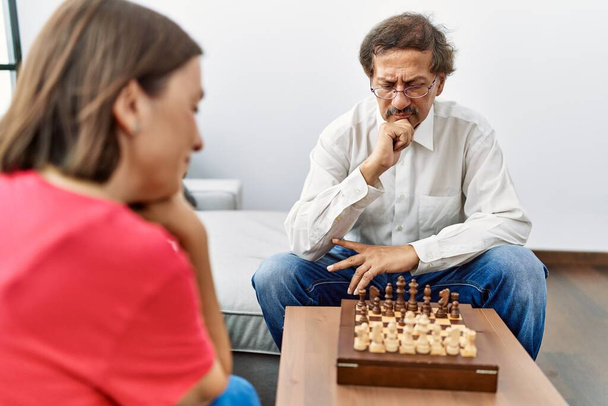 Middelbare leeftijd man en vrouw paar concentreren schaken thuis - Foto, afbeelding