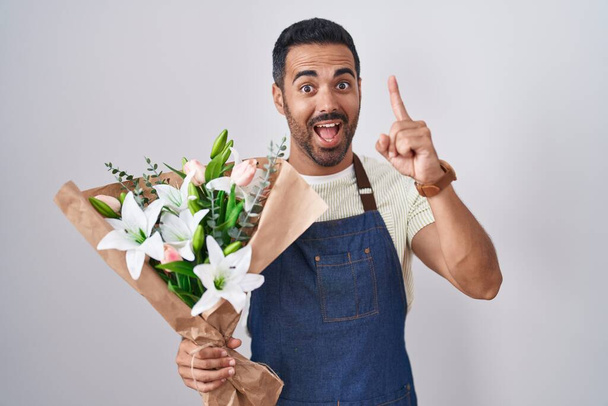 Een Spaanse man met een baard die als bloemist met een succesvol idee wijst. opgewonden en gelukkig. Nummer een.  - Foto, afbeelding