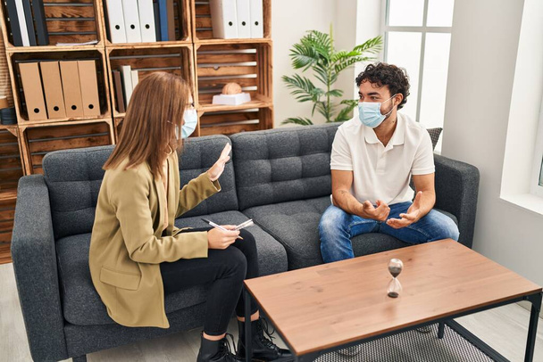 Man and woman wearing medical mask having psychology session at psychology center - 写真・画像