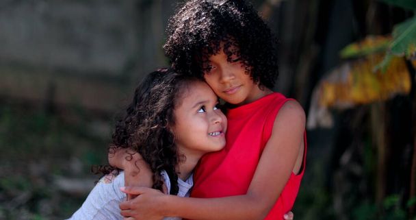 Τα παιδιά αγκαλιάζονται. Δύο μικρά Ισπανόφωνα κορίτσια αγκαλιάζονται - Φωτογραφία, εικόνα