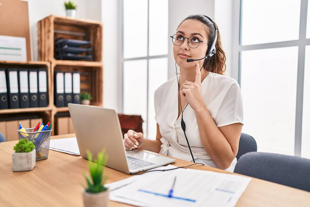 Young hispanic woman wearing call center agent headset at the office serious face thinking about question with hand on chin, thoughtful about confusing idea  - Zdjęcie, obraz