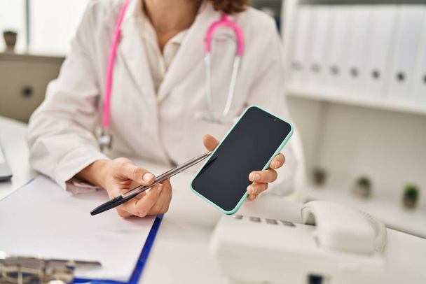 Young caucasian woman wearing doctor uniform showing smartphone screen at clinic - Photo, image