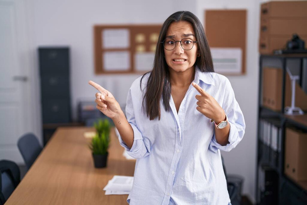 Ofisteki genç İspanyol kadın iki eliyle endişeli ve gergin bir ifadeye işaret ediyor.  - Fotoğraf, Görsel