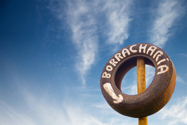 An old tire with the text: "Rubber shop", with the blue sky in the background and some clouds. - Photo, Image