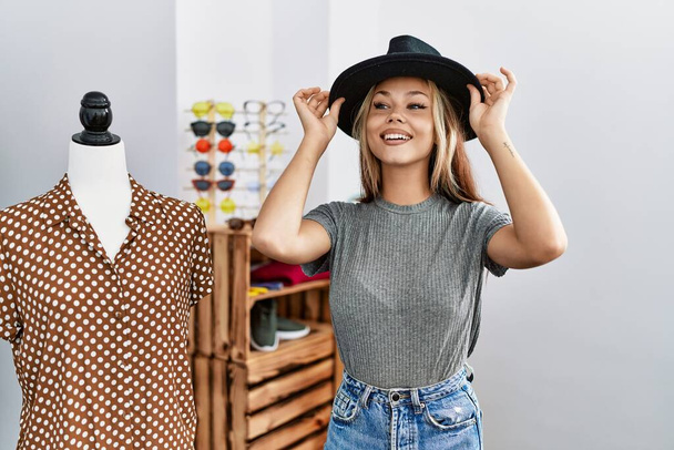 Молода біла жінка-клієнт посміхається щасливим капелюхом в магазині одягу
. - Фото, зображення