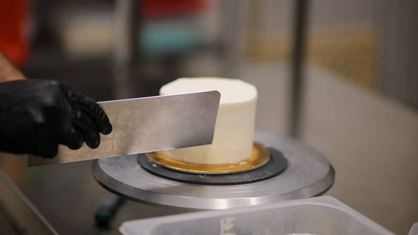 Decoratore con spatola e raschietto per lisciare la crema di burro su una torta glassata - Foto, immagini