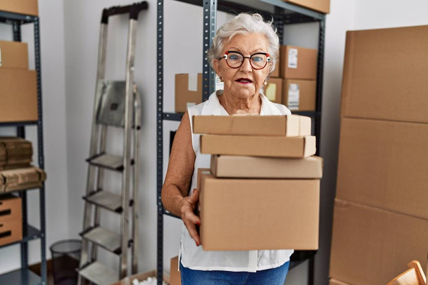 Ältere grauhaarige Unternehmerin hält Pakete im Büro - Foto, Bild