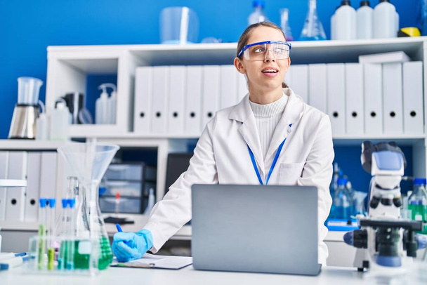 Молодая женщина ученый улыбается уверенно с помощью ноутбука в лаборатории - Фото, изображение