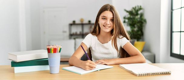 Adorable girl doing homework sitting on table at home - Fotografie, Obrázek