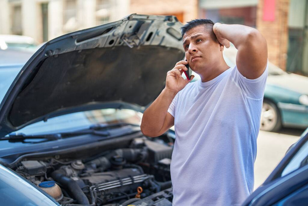 Young latin man talking on smartphone with insurance for car breakdown at street - Photo, image