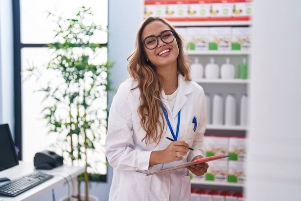 Молодая красивая латиноамериканка-фармацевт пишет на документе в аптеке - Фото, изображение