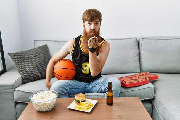 Fehér férfi hosszú szakállal tartja kosárlabda éljenzés tv játék nézi a kamera fúj egy csókot a kezét a levegőben, hogy szép és szexi. szerelem kifejezés.  - Fotó, kép