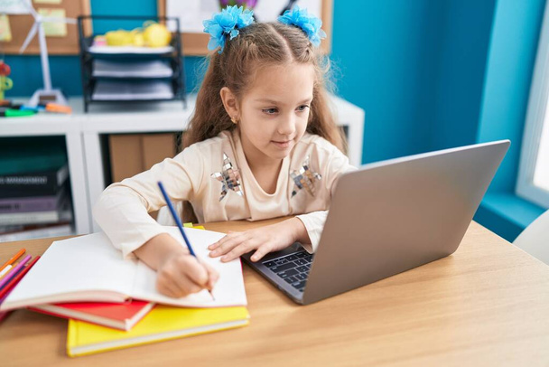 Adorable caucasian girl student using laptop writing on notebook at office - Foto, Imagen