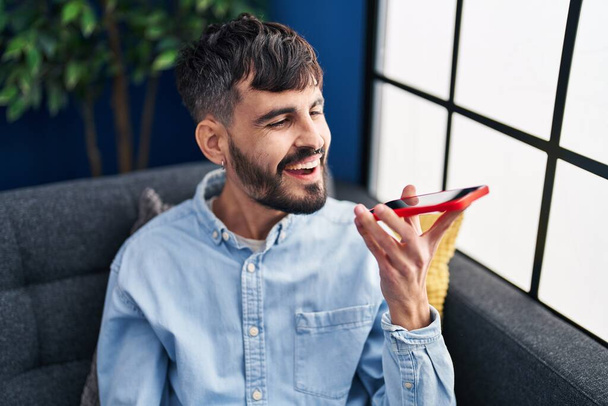 Young hispanic man talking on the smartphone sitting on sofa at home - Zdjęcie, obraz