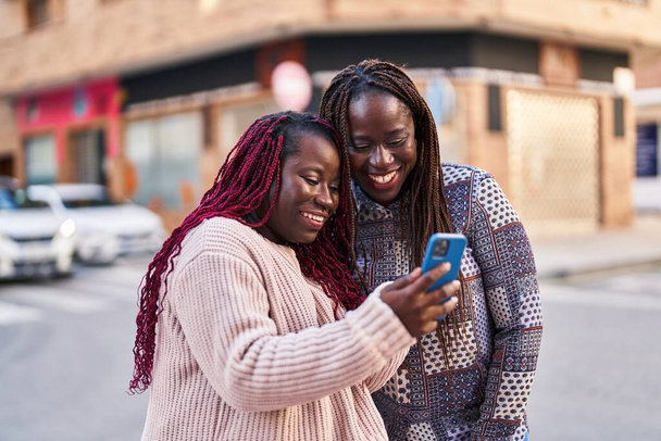 Afrikai amerikai nők barátok mosolygós magabiztos segítségével smartphone az utcán - Fotó, kép