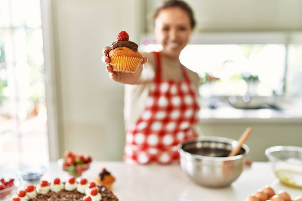 Fiatal gyönyörű spanyol nő mosolyog magabiztos gazdaság cupcake a konyhában - Fotó, kép