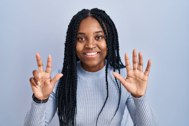 Mavi arka planda dikilen Afrikalı Amerikalı kadın 8 numaralı parmaklarıyla gülümseyerek kendinden emin ve mutlu bir şekilde işaret ediyor..  - Fotoğraf, Görsel