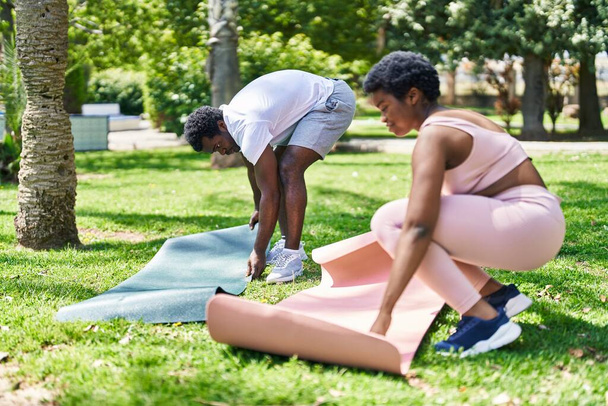 Africain américain homme et femme couple souriant confiant mettre tapis de yoga sur le sol au parc - Photo, image