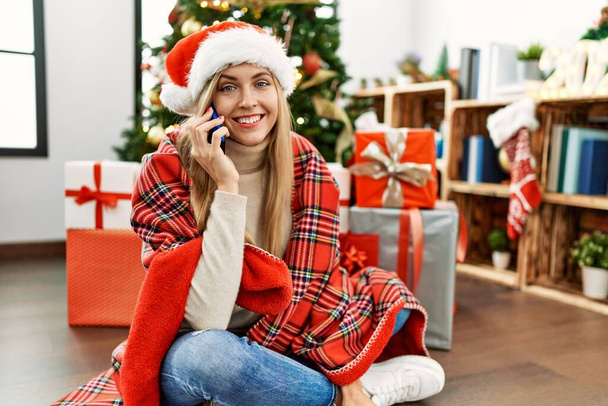 Mladá blondýna žena mluví na smartphone sedí u vánočního stromku doma - Fotografie, Obrázek