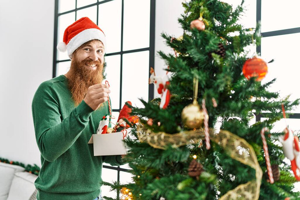 Young redhead man smiling confident decorating christmas tree at home - Foto, Bild