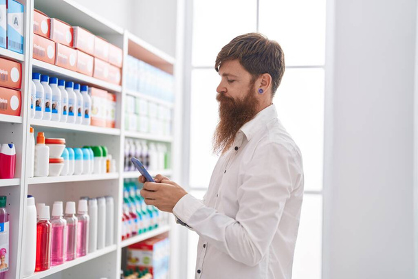 Young redhead man customer using smartphone at pharmacy - Foto, afbeelding
