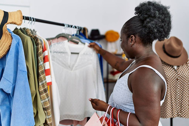 jong afrikaanse amerikaanse vrouw klant kiezen kleding van rack in kleding winkel - Foto, afbeelding