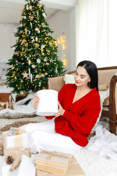Женщина держит коробку новогодних или рождественских подарков, указывая на камеру, вид спереди, крупный план, фон с копировальным пространством, для рекламы или текста - Фото, изображение