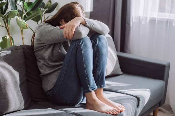 Unhappy anxiety young caucasian female covering face with knee sitting on sofa in living room at home, hurt heartbroken woman in depression feel desperate and anxious having psychological troubles - Foto, Imagem