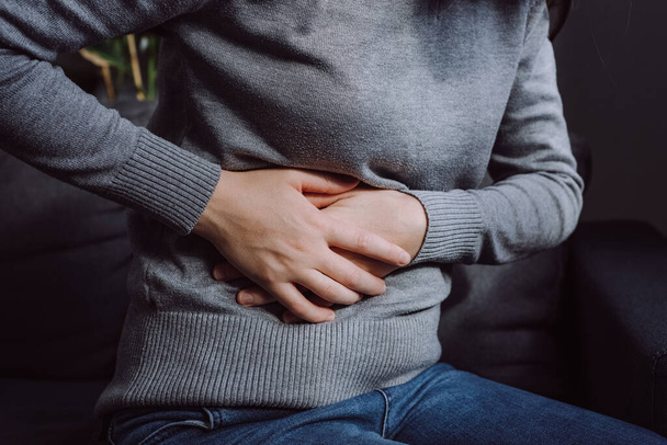 Flatulence young woman sitting on couch at home. Unhealthy girl suffer from food poisoning, abdominal pain and colon problem, gastritis or diarrhoea. Patient belly, abdomen or inflammation, concept - Foto, Imagen