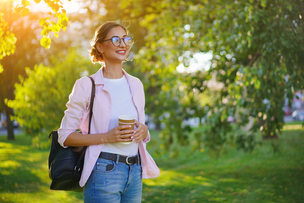 Businesswoman standing summer park Business person Outdoors Successful european caucasian woman freelancer or teacher walking outside with black backpack dressed denim jeans white shirt pink jacket - Foto, Imagem