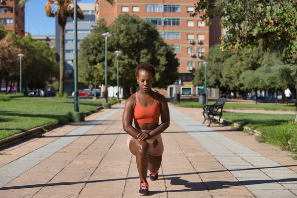 Femme afro-américaine en vêtements de sport effectuer des exercices d'étirement des jambes pour commencer à courir. Concept sport, course, bien-être, exercice, fitness. - Photo, image