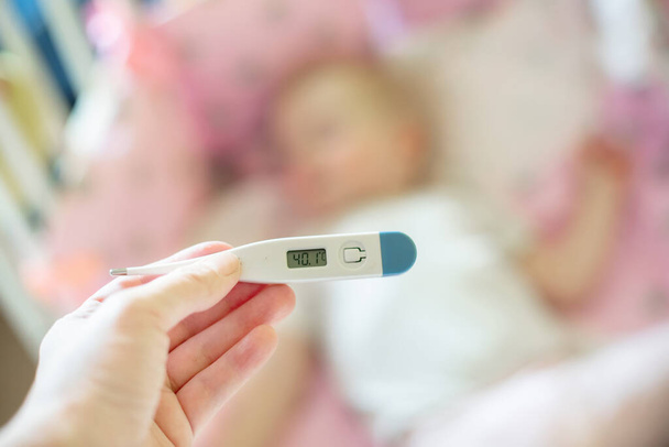 Medizinthermometer in Großaufnahme, Eltern messen Temperatur eines kranken Kindes, 1-jähriges Kleinkind bekommt hohes Fieber im Bett liegend. Fieber bei Kindern. - Foto, Bild
