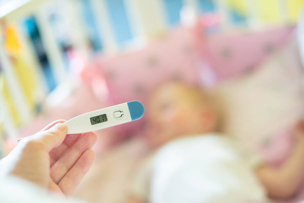 Κοντινό ιατρικό θερμόμετρο, γονική μέτρηση της θερμοκρασίας του άρρωστου παιδιού, 1 έτους κοριτσάκι παίρνει υψηλό πυρετό που βρίσκεται στο κρεβάτι. πυρετός στο παιδί. - Φωτογραφία, εικόνα