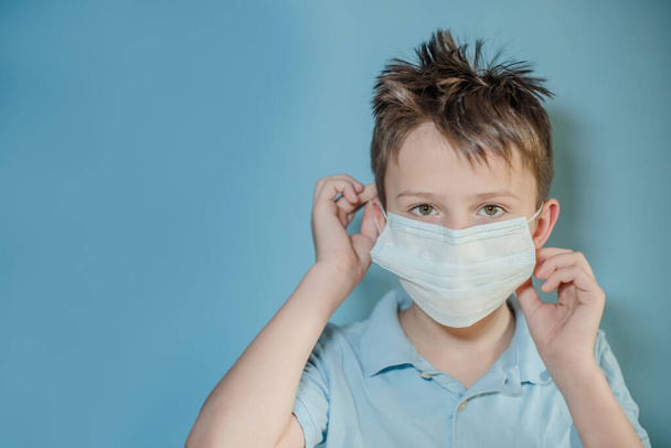 мальчик снимает защитную медицинскую маску с лица на синем фоне. ребенок с гриппом, хантавирусом или простудой защищен от вирусов, загрязнения в плохих эпидемических ситуациях, среди пациентов с коронавирусом - Фото, изображение