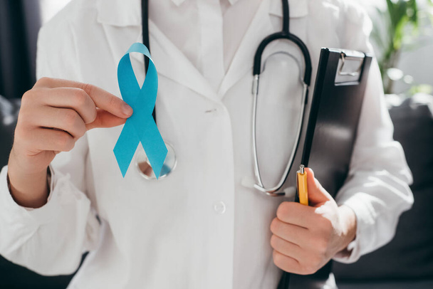 Профессиональная женщина-врач в форме со стетоскопом, держащая светло-голубую ленточку и планшет. Кампания по повышению осведомленности о здоровье мужчин и раке предстательной железы в ноябре. Символ медицинских проблем - Фото, изображение