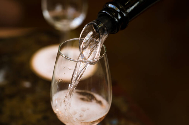 Witte mousserende wijn uit een fles wordt in een glazen beker gegoten. Wijn degustatie. Close-up. - Foto, afbeelding