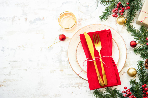 Weihnachtsessen, weihnachtliche Tischdekoration mit weißem Teller, goldenem Besteck und Weihnachtsdekoration auf hellem Holzgrund. Ansicht von oben. - Foto, Bild