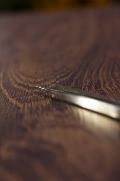 Silver eyelash extension tweezers close-up on a wooden background - Valokuva, kuva