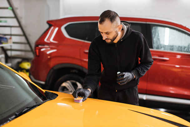 Young man, car polish service worker polishing car hood, buffing and polishing yellow luxury sport vehicle with nano ceramic composition or wax. Car detailing. Tools for polishing. - Fotó, kép