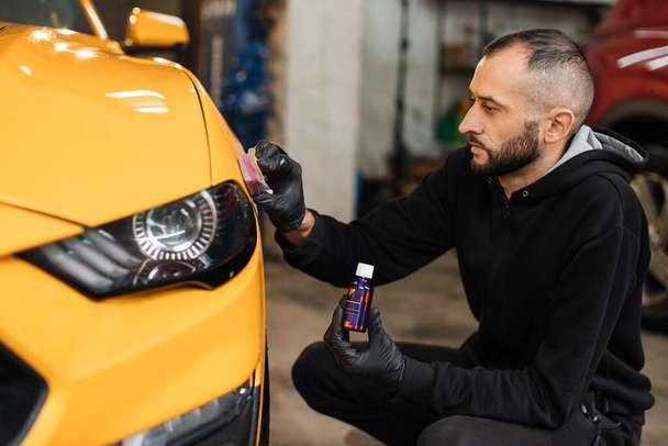 Skillful and professional male auto service worker polishing and detailing a car body, waxing yellow sport car hood and headlight with a wax or nano ceramic coating. Car wash service - Photo, image