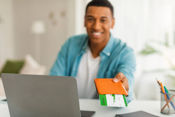 Happy millennial african american man manager with laptop giving passport and airline tickets to client in office interior, blurred. Successful trip, travel, vacation and holiday after covid-19 - Photo, Image