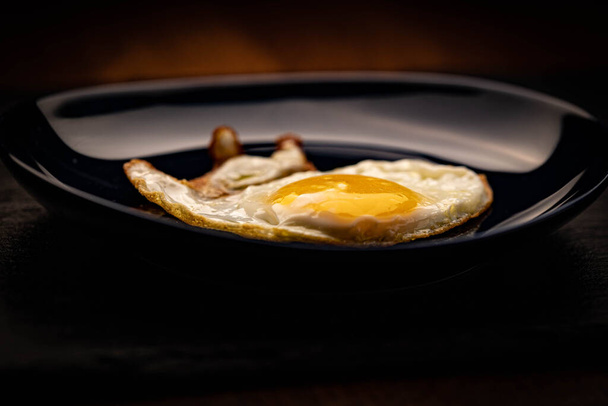 Ηλιόλουστο τηγανιτό αυγό σε σκούρο πιάτο - Φωτογραφία, εικόνα