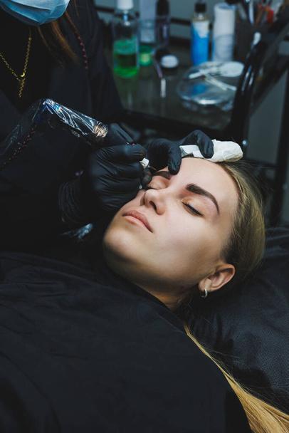 Beautician hand doing brow permanent makeup on an attractive female face - Fotó, kép