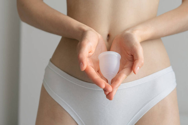 A white menstrual cup lies in the hands of woman on an isolated background. Theme of menstruation and critical days. Hygienic silicone bowl for menstrual blood. Reusable alternative to pads - Foto, Imagen