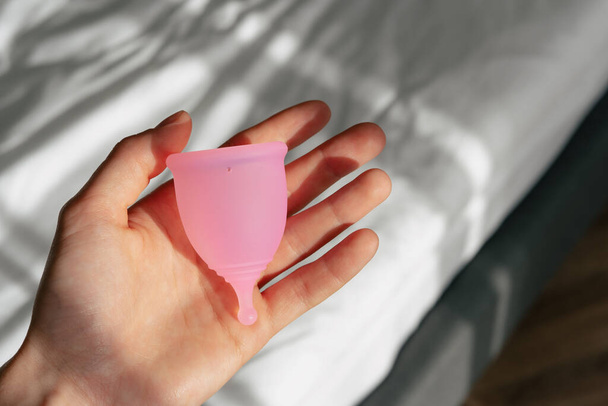 Розовая менструальная чашка лежит в руке женщины. Гигиеническая альтернатива менструальным прокладкам - Фото, изображение