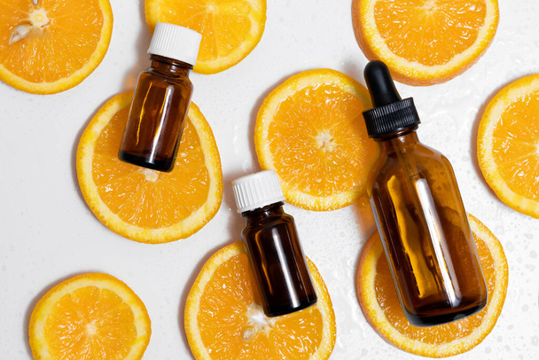brown jars of oil and serum lie on round pieces of orange with water drops. summer and freshness concept - Foto, afbeelding