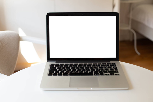 ноутбук стоит на столе с белым чистым экраном в интерьере квартиры. макет для вашего дизайна - Фото, изображение
